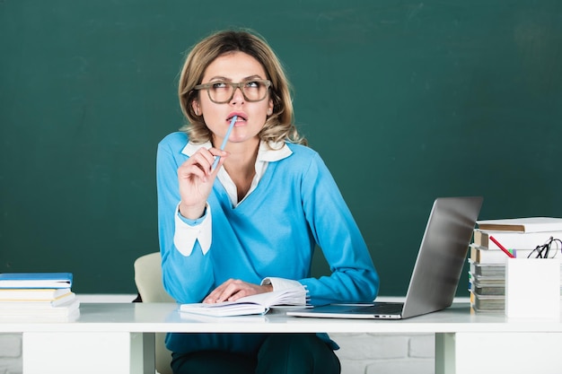 Modern attractive teacher Portrait of smart young woman in glasses with book on the blackboard in class at high school or collage Female student study in university Education school and people