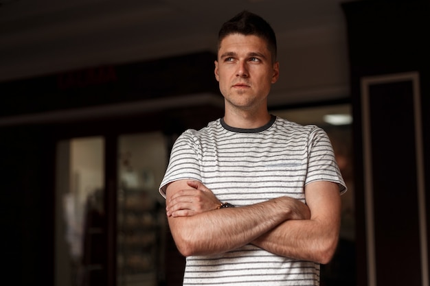 Modern attractive young man in a fashionable striped t-shirt with a stylish hairstyle posing in a dark studio.