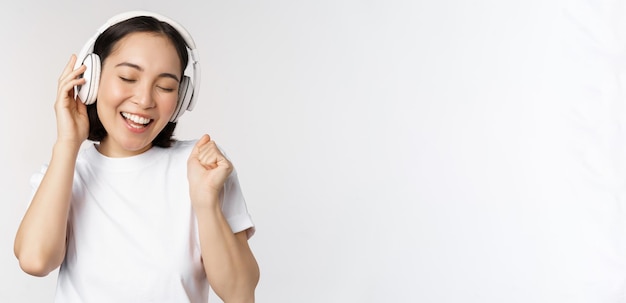 Modern Aziatisch meisje dansen luisteren muziek met koptelefoon glimlachend gelukkig staan in tshirt op witte achtergrond