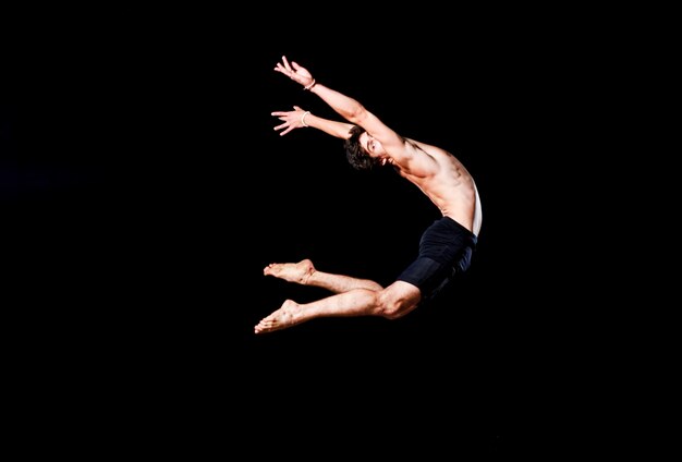 Modern ballet style male dancer performs on high lighted stage .