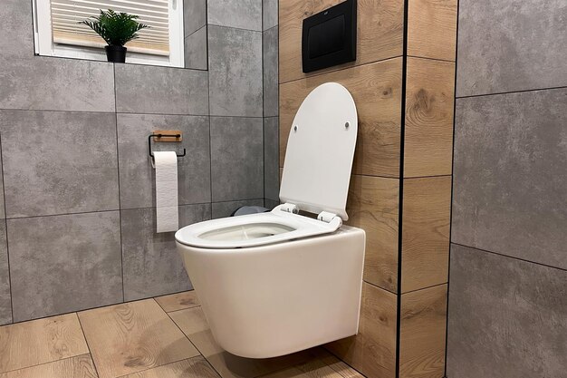 A modern bathroom with a ceramic toilet in white The toilet is closed and has a seat and a flush The bathroom has a wall and a floor with tiles