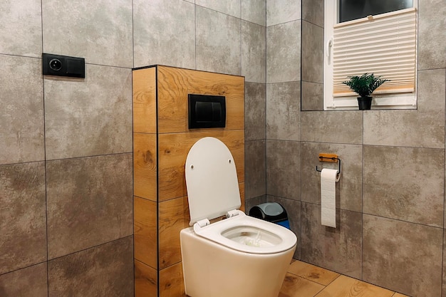 A modern bathroom with a white ceramic toilet The toilet is closed and has a stylish seat and a flush The bathroom has a wall and a floor made of tiles