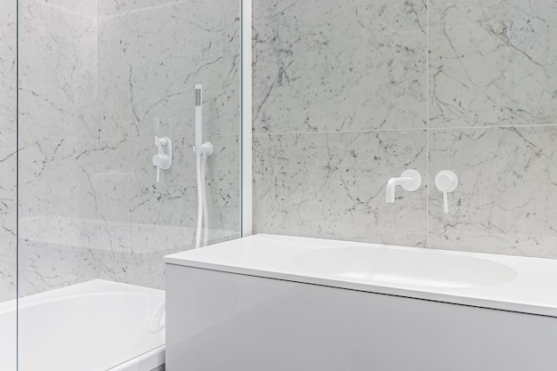 Modern bathroom with white faucets and shower walls lined with white marble