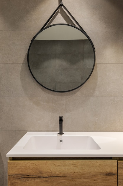 Bagno moderno con lavabo bianco base in legno e specchio tondo stile minimalista interior design in guerra...