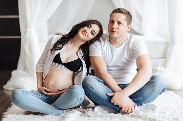 modern beautiful pregnant woman in jeans and shirt with her husband at home Concept of pregnancy motherhood preparation and waiting The beauty of a woman during pregnancy