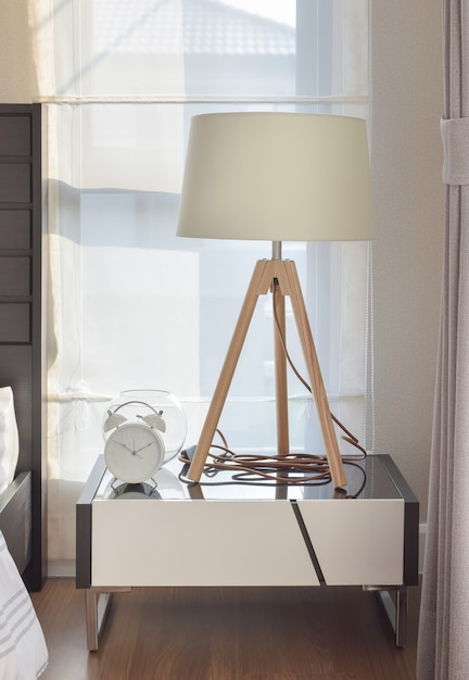 Modern bedroom interior with wooden lamp and alarm clock on bedside table