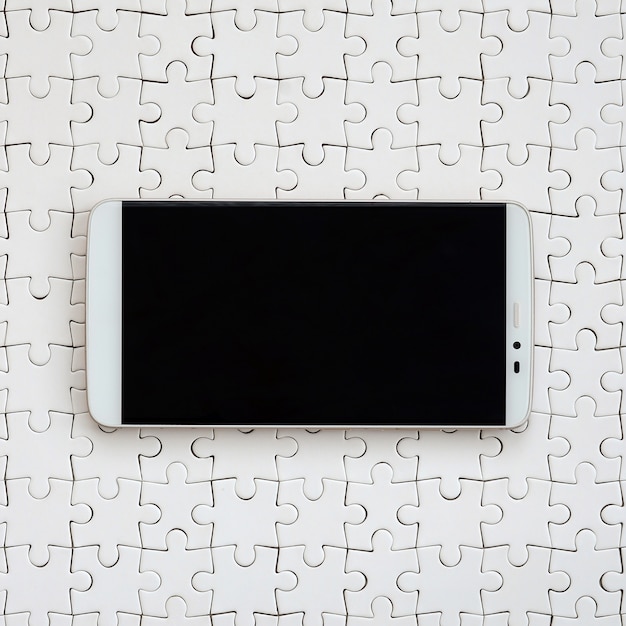 A modern big smartphone with a touch screen lies on a white jigsaw puzzle in an assembled state