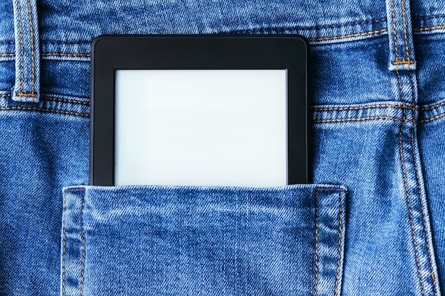 A modern black electronic book with a blank screen in the back pocket of bright blue jeans.