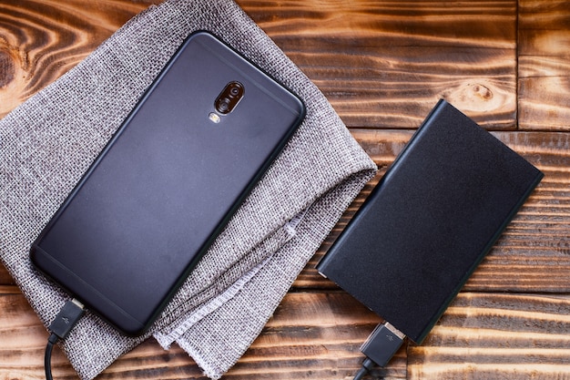 modern black smartphone  and a connected power bank on a wooden background.