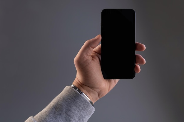 コピースペースで垂直に灰色の背景の電話画面に男性の手で現代の黒いスマートフォン