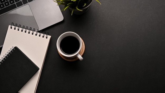 Vista superiore moderna dell'area di lavoro nera con il blocco note a spirale del computer portatile del caffè e lo spazio della copia