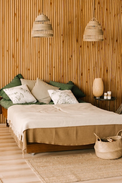 Современный интерьер спальни в стиле бохо с деревянными ламелями, плетеными светильниками, изумрудным текстилем