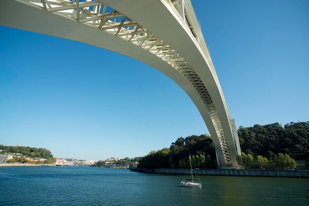 Modern bridge over sailboat moving on river against clear sky