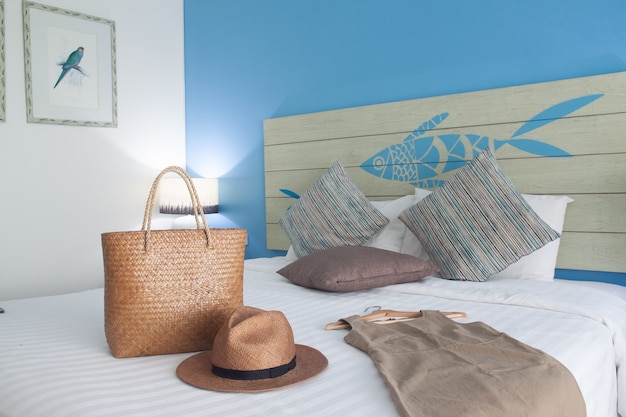 Фото Современная светлая спальня с летней одеждой, платьем, шляпой и сумкой на белой кровати.