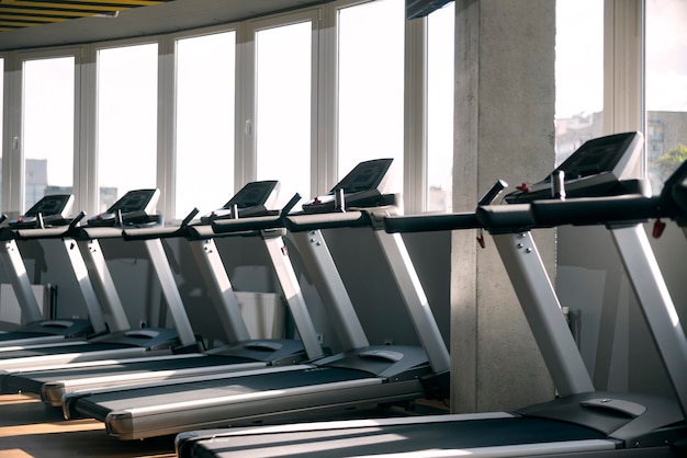 Modern bright gym. Treadmills near the windows. Sports simulators for running. Fitness equipment.