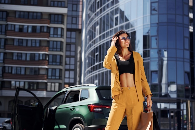Современное бизнес-здание на заднем плане Молодая модная женщина в бордовом цветном пальто днем со своей машиной