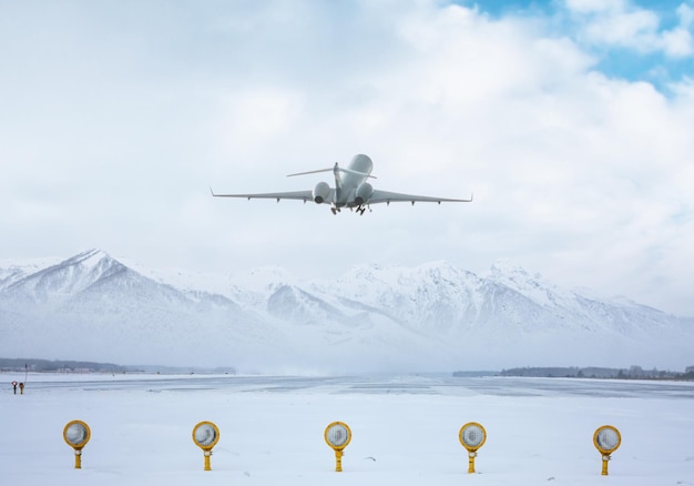 현대적인 비즈니스 제트기는 아름다운 눈 덮인 산을 배경으로 공항 활주로에서 이륙합니다.