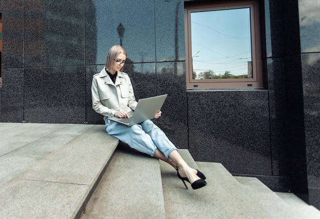 Modern business lady sitting on the stairs with laptop near the business center Freelance Remote Work Lifestyle