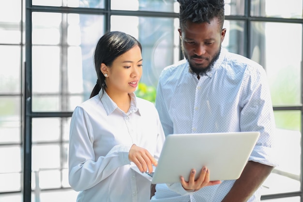 Gli uomini d'affari moderni stanno lavorando utilizzando il laptop e sorridendo mentre sono in piedi in ufficio