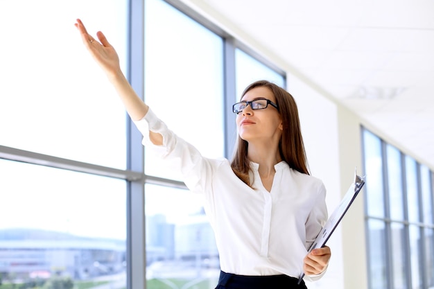 Modern business woman points up by her hand while standing in the office