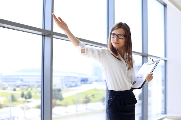 Modern business woman points up by her hand while standing in the office