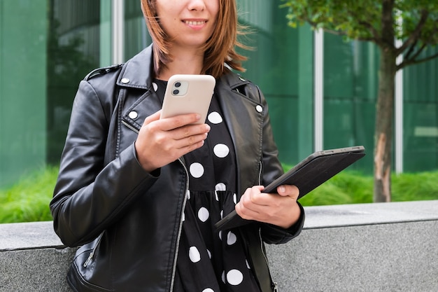 Современная деловая женщина с телефоном и планшетом в руках ждет клиента на улице рядом
