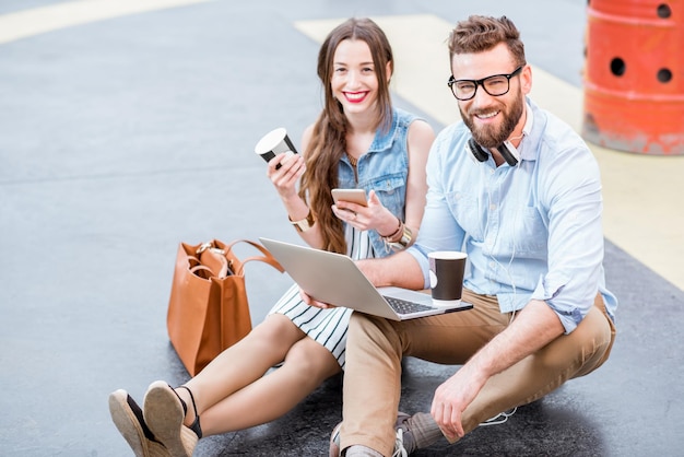 Modern businessman and businesswoman working with laptop and coffee outdoors on the heliport ground. Lifestyle business concept