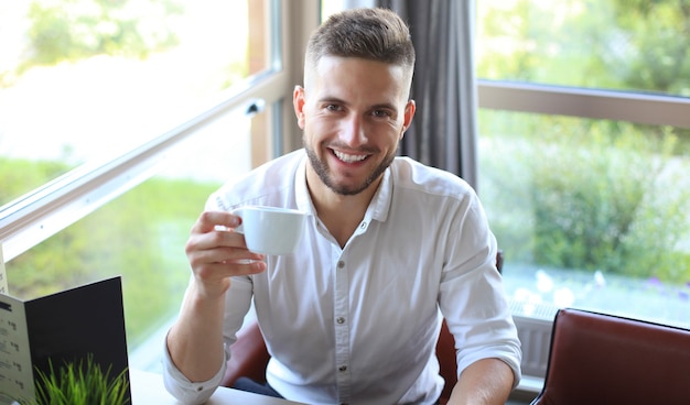 Modern businessman drinking coffee in the office cafe during lunch time and using laptop