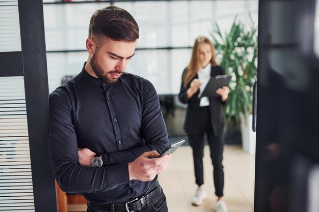 オフィスの屋内に立っている現代のビジネスマン。後ろにいる彼の女性の同僚。