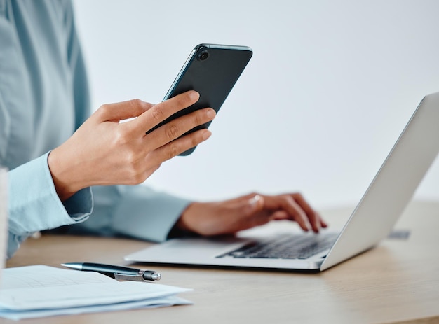 Modern businesswoman texting on phone and laptop while working reading and planning strategy indoors Closeup of a productive corporate worker multitasking on multimedia technology and app software