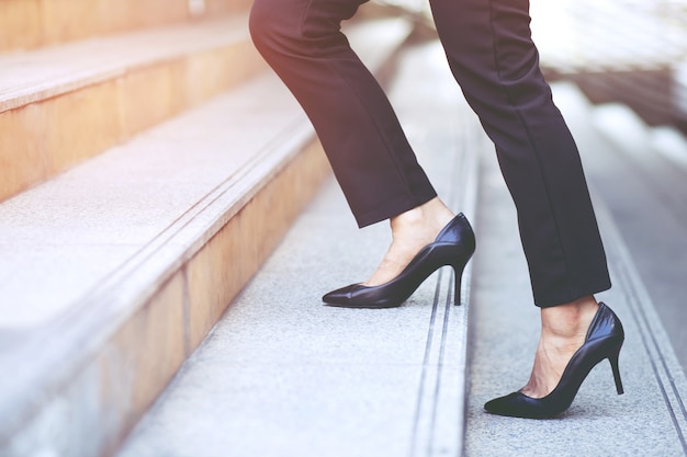 現代の実業家の働く女性は、急いでオフィスで働くためにラッシュアワーに近代的な都市の階段を歩いて足を閉じます。