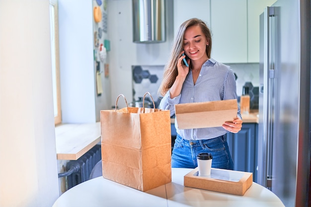 Modern busy casual cute adult happy smiling young woman customer received cardboard bags with takeaway food and drinks at home. Fast delivery service concept