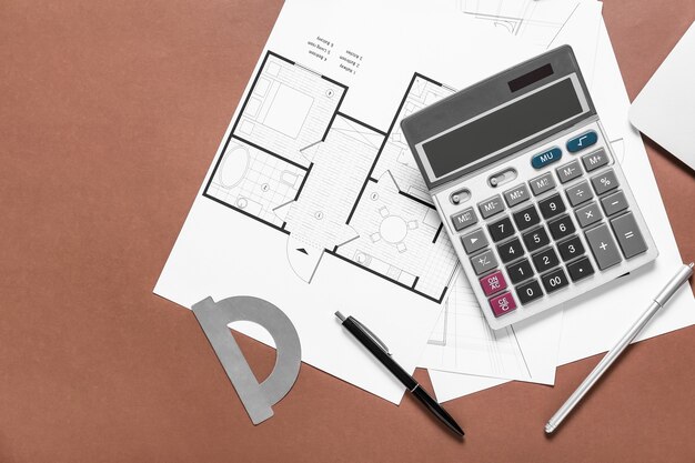 Modern calculator with house plans and stationery on color surface