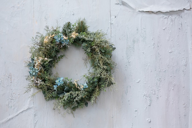 Modern christmas wreath. stylish rustic christmas wreath with\
pine cones,fir branches,snow, hanging on white wall. space for\
text. handmade decor for winter holidays