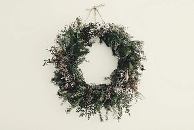 Modern Christmas wreath stylish rustic christmas wreath with pine conesfir branchessnow hanging on white wall space for text handmade decor for winter holidays