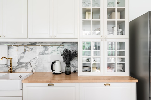 Фото Современный классический кухонный интерьер с кухонной техникой и белой керамической раковиной с золотым зеркальным смесителем на деревянной поверхности с мраморной стеной
