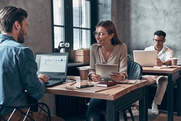 modern colleagues in smart casual wear communicating together and using technologies 