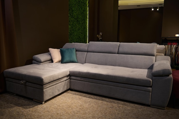 Modern comfy soft upholstered gray sofa with green and beige pillows in the exhibition hall of furniture shop