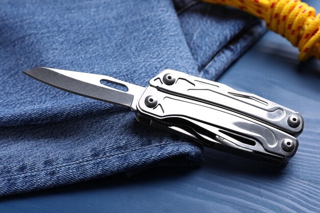 Modern compact portable multitool and jeans on blue wooden table