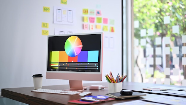 Modern computer pc with color chart on monitor screen coffee cup and stationery at design studio