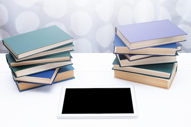 A modern computer tablet and stacks of books on a white wooden table