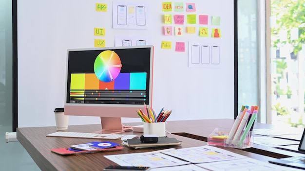 Modern computer with color swatches and wireframe sketches for mobile application on wooden table