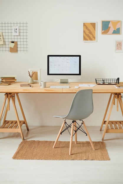 Modern computer with online calendar on screen placed on wooden desk against wall with pictures in o