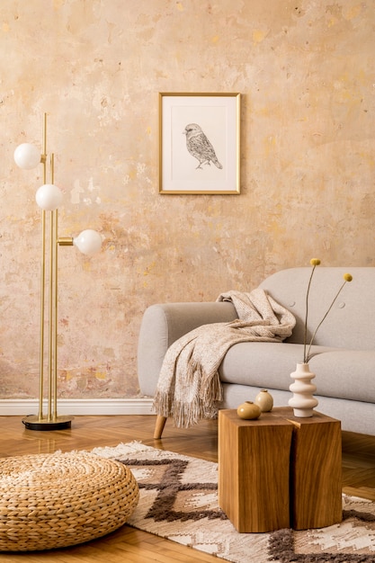 Современная концепция интерьера гостиной с золотой лампой, дизайнерским серым диваном, пуфом из ротанга, макетом фоторамки, сушеным цветком.