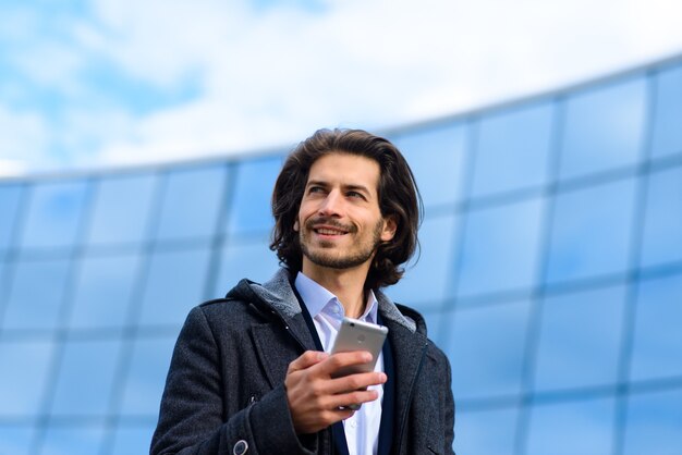 Современный уверенный молодой бизнесмен в полном костюме, стоящий на открытом воздухе с городским пейзажем на заднем плане