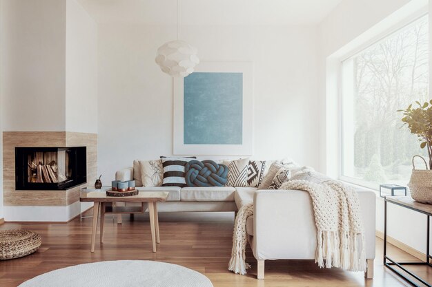 Modern corner fireplace in a sunny peaceful living room interior with white walls and cozy pillows and blankets on a beige sofa