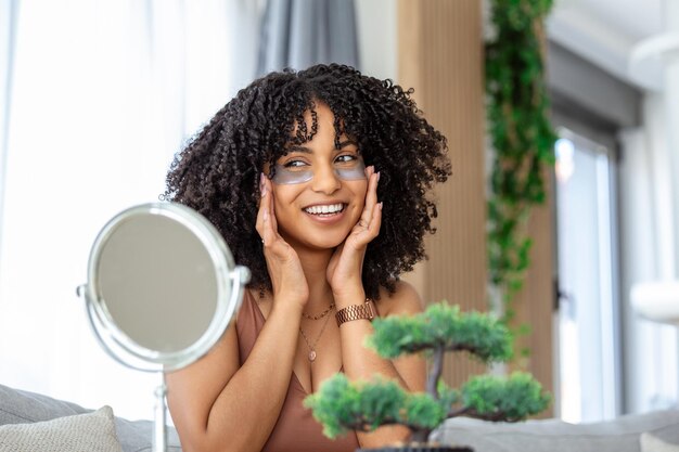 Modern cosmetology and patches against fatigue under the eyes Cheerful young african american woman applying them under her eyes