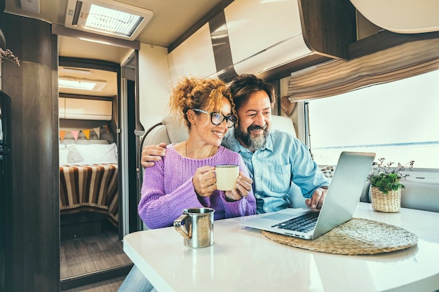 Modern couple use together laptop inside camper van computer\
leisure people surfing the web traveler planning next destination\
smiling and enjoying freedom living off grid digital nomad\
concept