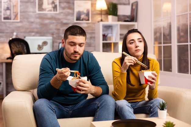 Nel moderno e accogliente soggiorno, la coppia si sta godendo i noodles da asporto mentre guarda la tv comodamente sul divano