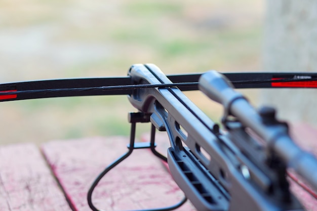 A modern crossbow with arrows and a telescopic sight lies on a wooden table in the street. Preparing for the hunt.